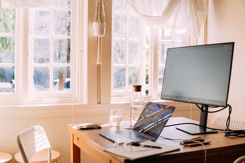 A latop sits on a desk below computer screen.